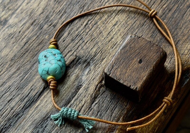 UNIRELIC | Verdant Vein Relic  “Within its veins, the stone remembers how it grew toward the light.”  Materials  Core Stone: Natural blue jadeized turquoise with visible growth veins  Cord: Hand-braided waxed cowhide leather  Metal Accent: Antique brass bead  Design Meaning This turquoise is not flawless — and that is its beauty. Its natural veins flow like branches stretching toward sunlight, a silent record of its formation within the earth. The blue-green hue mirrors the meeting of sky and forest — blue for clarity and calm, green for vitality and renewal. The veins are not cracks, but traces of energy in motion, reminding the wearer that growth itself is perfection in progress.  Energy & Symbolism Since ancient times, turquoise has been revered as a bridge between heaven and earth, a talisman of harmony, emotional balance, and spiritual protection. Its natural patterns embody the rhythm of life, guiding the soul to breathe in sync with nature — steady, open, and aware.  Craftsmanship Hand-braided with waxed cowhide leather for a warm, grounded texture. Each knot is tied through intention and stillness, symbolizing connection and protection. The turquoise remains in its organic form, untouched by heavy polish — authentic, serene, and alive with ancient breath.  Dimensions  Length: ___ mm  Width: ___ mm  Height: ___ mm (Handcrafted; slight variations are natural and unique.)  For the Wearer  Seekers of peace, balance, and mindful living  Lovers of raw natural stones and organic textures  Those who honor growth and transformation as a sacred process  A meaningful gift symbolizing life, strength, and renewal